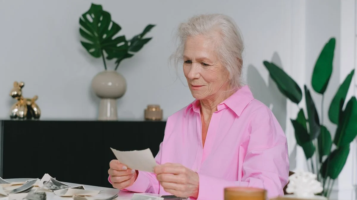 An elderly woman sitting at a kitchen table holding a vintage locket in her palm, reminiscing