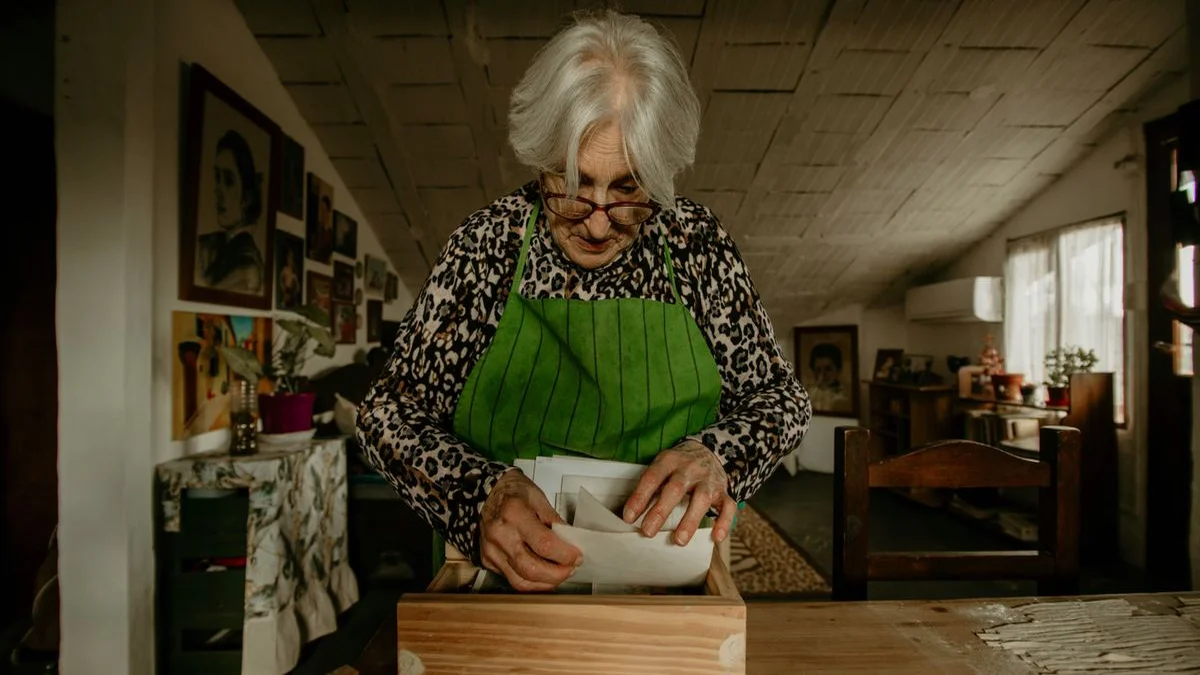 A person sits at a wooden kitchen table sorting through a stack of handwritten recipe cards in warm afternoon light