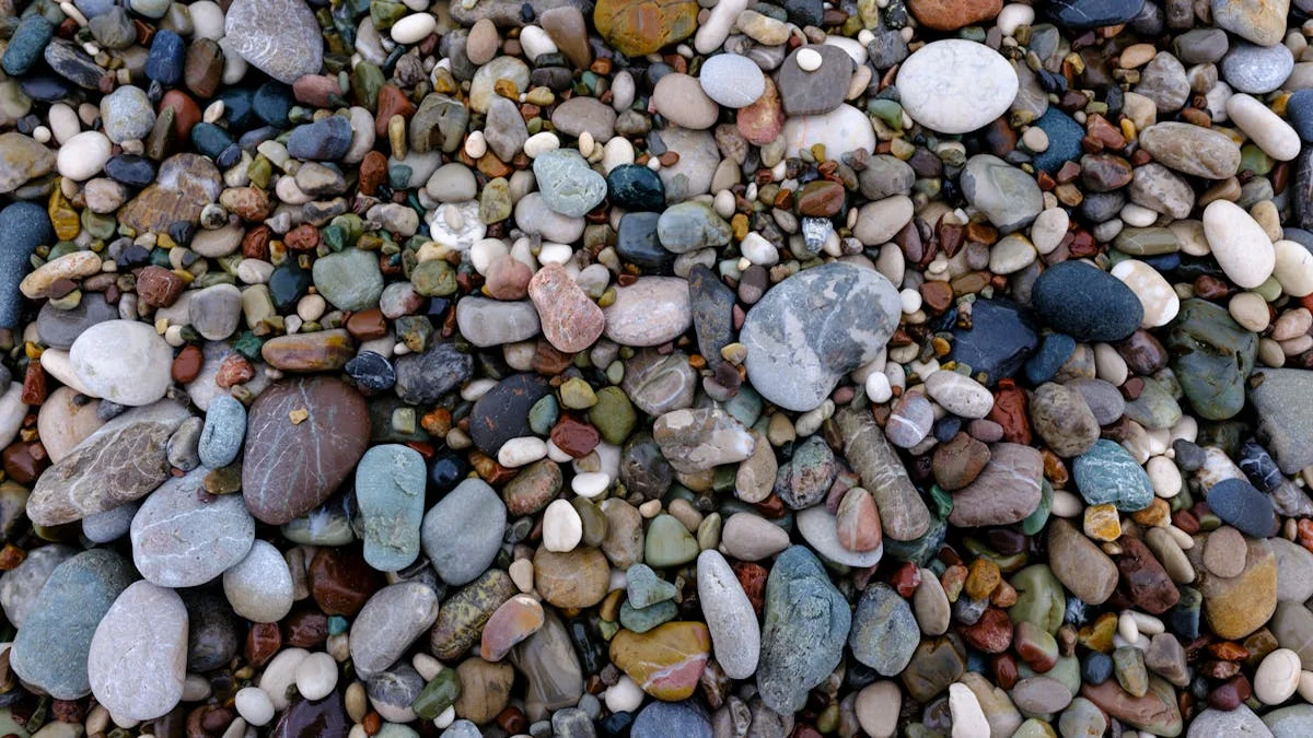 A child's hand holding a collection of varied, colorful rocks against a backdrop of dirt and leaves