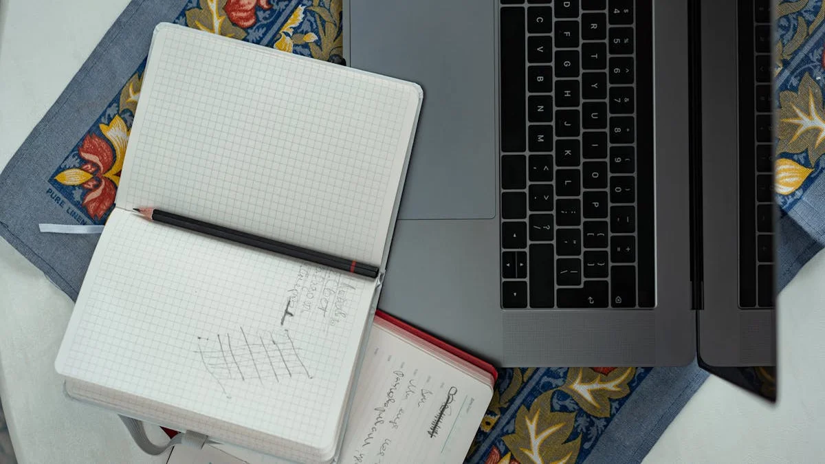 A laptop open to a simple pixel grid next to a sketchbook